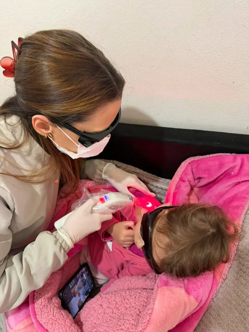 Laserterapia em atendimento domiciliar em Porto Alegre, com a criança no colo e protegida por óculos